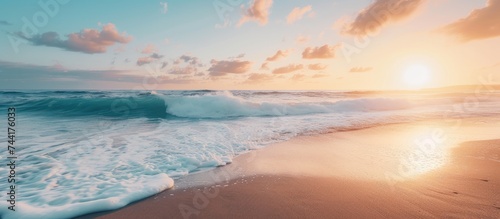 The sun is seen descending below the horizon, casting a warm glow over the gently crashing ocean waves.