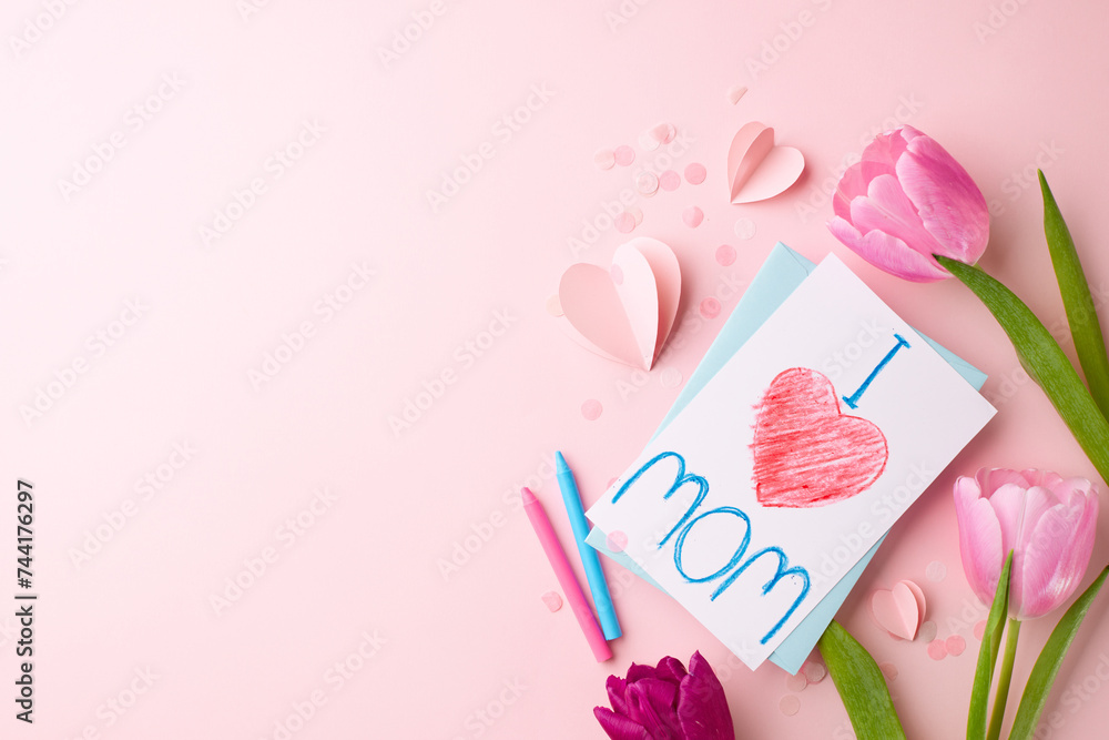 Crafted with love: a mother's day homage. Top view shot of pink tulips, a child's drawing saying 'I love mom', crayons, paper hearts on soft pink background with space for sweet dedications Crafted with love: a mother's day homage. Top view shot of pink tulips, a child's drawing saying 'I love mom', crayons, paper hearts on soft pink background with space for sweet dedications