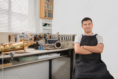 Musical instrument repairer looking into camera with saxophones on his workbench