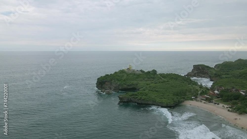 Aerial view of fish monument on the huge coral rock on Krakal Beach. Drone moving forward. Reveal drone shot. Tropical Beach. Indonesia. photo
