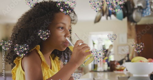 Image of flower hearts over african american girl drinking juice at home