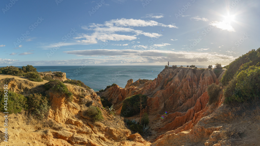 Tourist standing on golden rock cliffs at the coastline of the Atlantic Ocean with near the Cave of Benagil, Algarve, Portugal