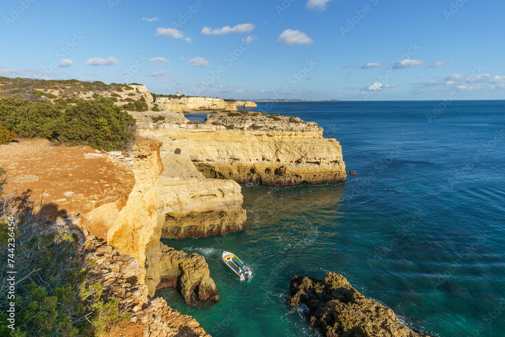Boat on the sea in front of the golden cliffs at the atlantic coast line near Benagil cave, Algarve, Portugal. Boat on the sea in front of the golden cliffs at the atlantic coast line near Benagil cave, Algarve, Portugal.