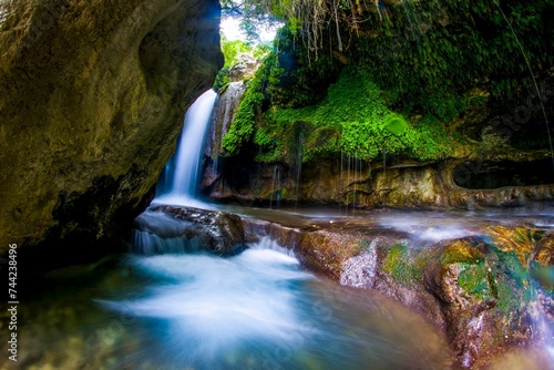 Tranquil landscape featuring a small waterfall cascading down a rocky cliff side. © Wirestock