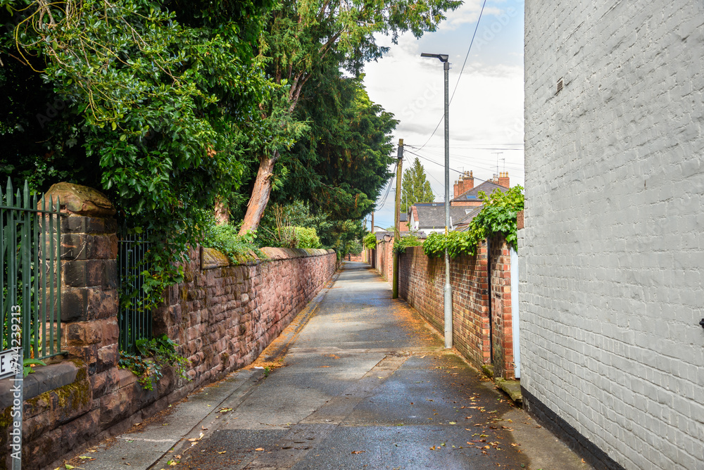 Empty narrow street running between a stone and brick walls in a residential district on a sunny summer day