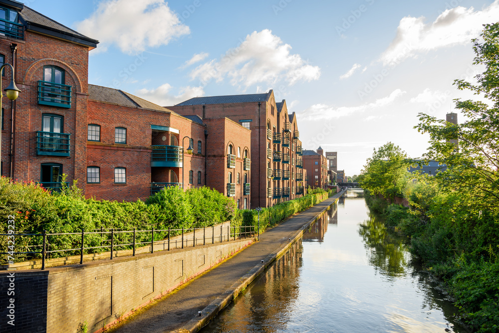 Brick apartment buildings and converted warehouses in a redevelopment along a canal at sunset. Afootpath lines the canal.