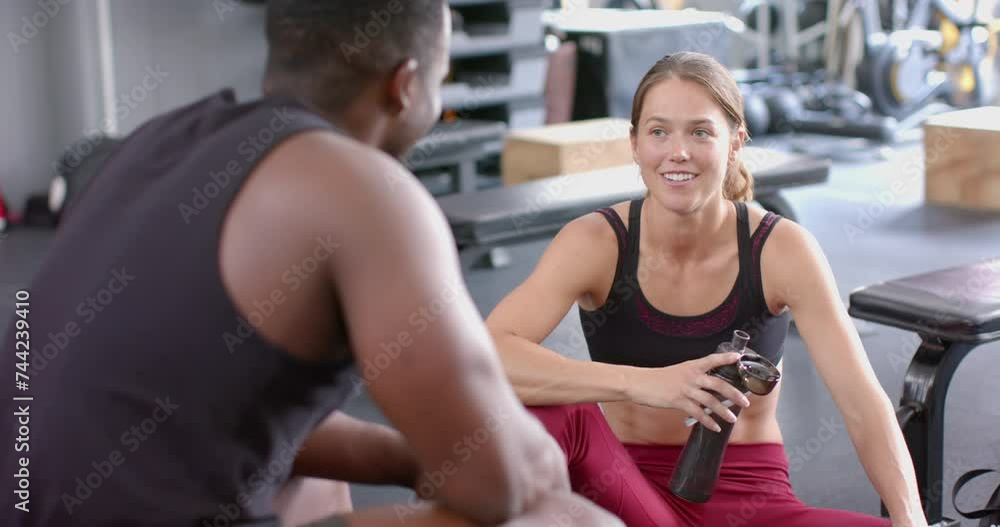 Fit young Caucasian woman chats with an African American man at the gym Fit young Caucasian woman chats with an African American man at the gym