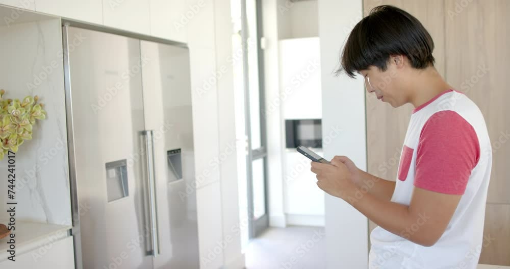 Teenage Asian boy focused on his smartphone at home in the kitchen with copy space Teenage Asian boy focused on his smartphone at home in the kitchen with copy space