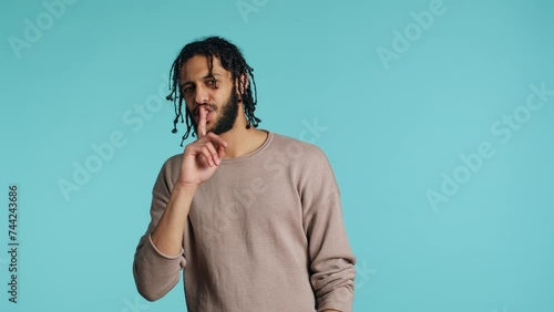 Annoyed middle eastern man doing shushing hand gesturing, irritated by noise, having negative mood. Assertive person placing finger on lips, doing quiet sign gesture, studio background, camera A photo
