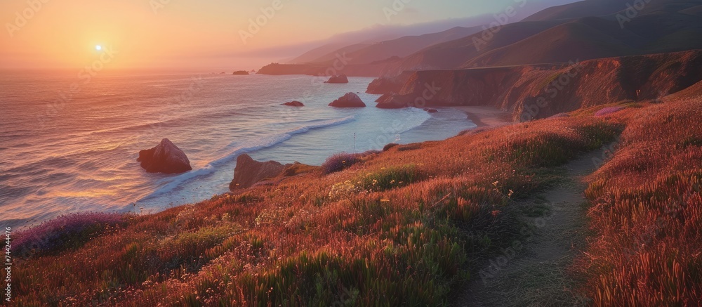 Dusk in Big Sur showcases the breathtaking gradient of sunset colors as the sun descends over the ocean near a majestic cliff.