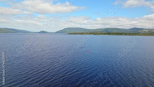 Aerial view dolly in of two people kayaking on huillinco lake in Chiloe, Chile. Clear horizon on a sunny day photo