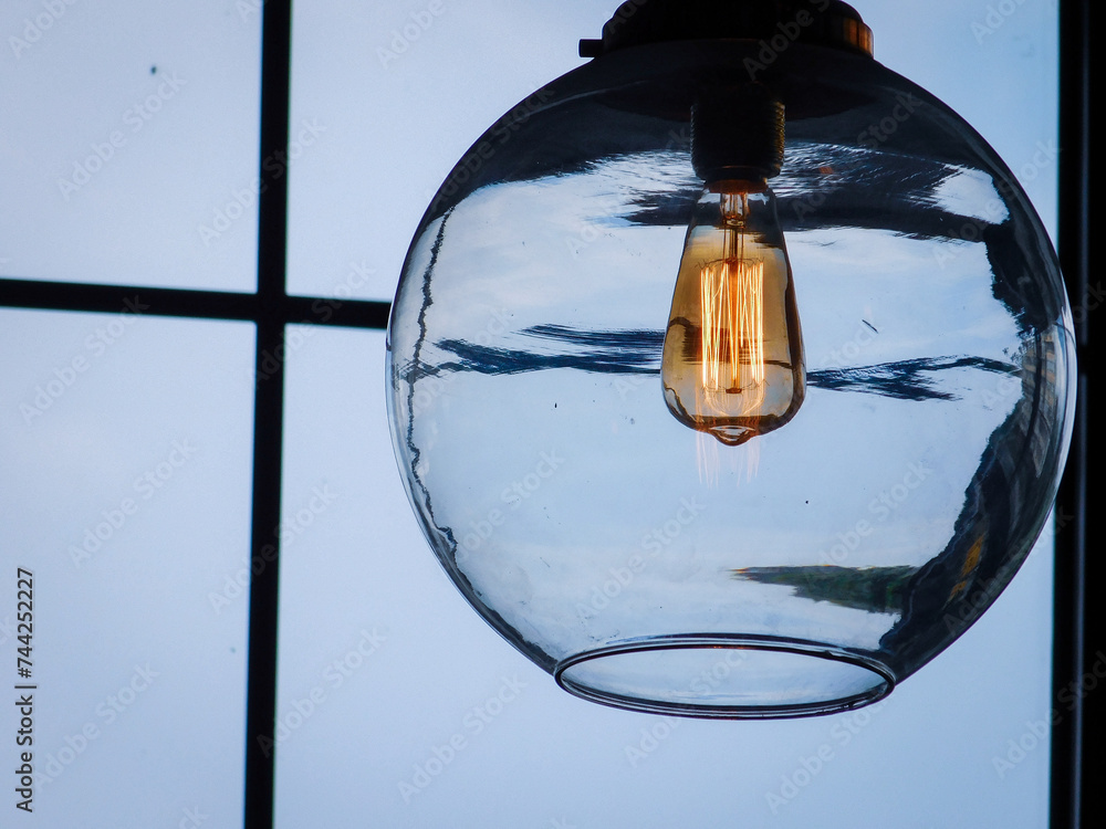 a clear light bulb hanging from a ceiling lamp near a window