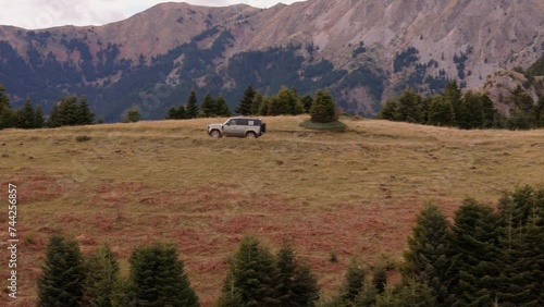 Aerial sideview of SUV driving between grassy dirt road in mountains, pan to track and follow photo