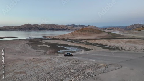 black pick truck driving along a dried lake bed at dusk with his lights on in Millerton Lake Fresno California 60fps photo