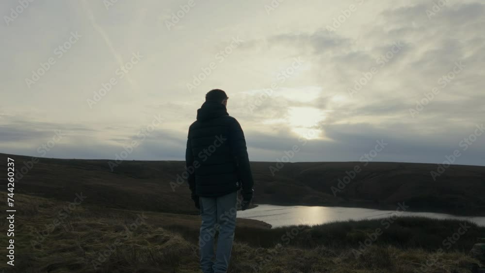 Young boy standing and looking out on to the winter landscape, with moorlands, fens, a lake and stormy winters sky. Sunset view of the Yorkshire landscape Young boy standing and looking out on to the winter landscape, with moorlands, fens, a lake and stormy winters sky. Sunset view of the Yorkshire landscape