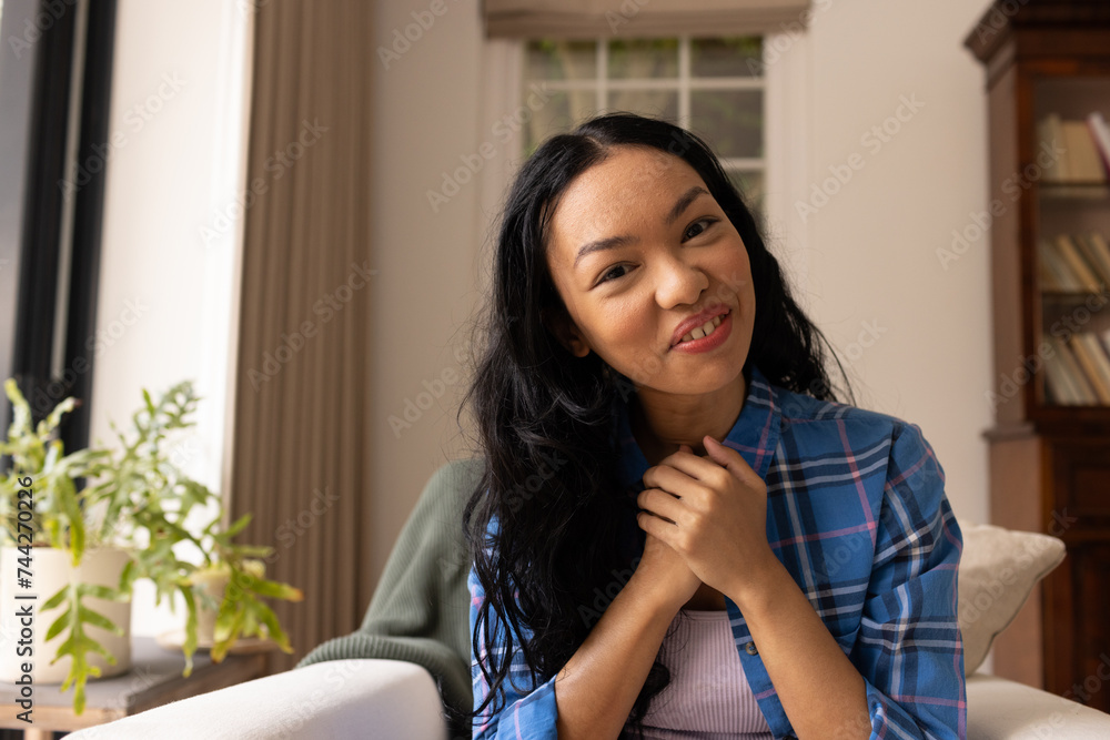 A young biracial woman smiles warmly on video call, seated indoors A young biracial woman smiles warmly on video call, seated indoors