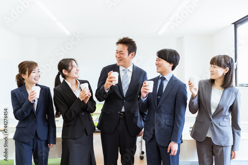 コーヒーを飲みながら充実した笑顔で談笑するビジネスマンとビジネスウーマン（アジア人・日本人の男女） 
