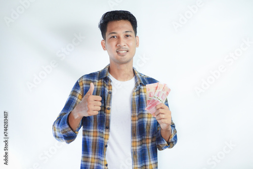 Closeup portrait of adult Asian man give thumb up while holding money and showing happy face expression photo