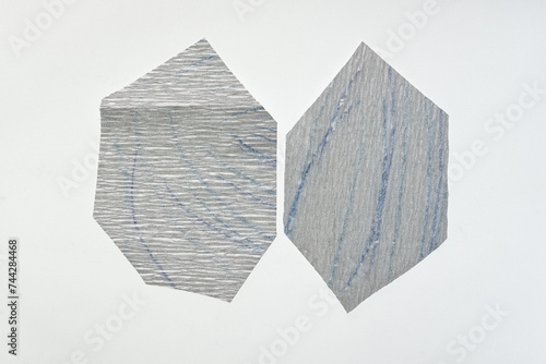two irregular hexagonal metallic silver crepe paper shapes on a blank surface