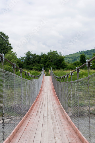 A new wooden bridge over a mountain river on cables. Ukrainian Carpathian Mountains. A bridge over a mountain river. Green grass and trees. © Ольга Семенів