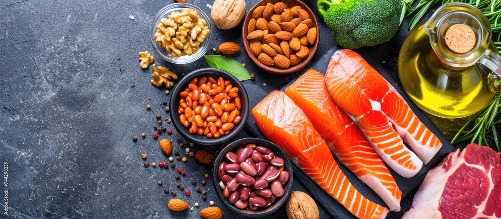 A top view image showcasing a variety of healthy keto diet food products, such as salmon steak, beef, beans, nuts, vegetables, and olive oil, neatly arranged on a black stone table.