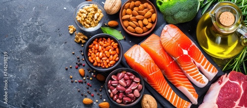A top view image showcasing a variety of healthy keto diet food products, such as salmon steak, beef, beans, nuts, vegetables, and olive oil, neatly arranged on a black stone table.