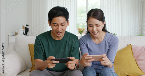 Young adult asia cute sweet couple enjoy playing sport match game online in esport race lover at home sofa couch. Two Gen Z people man and woman gamer happy relax smile laugh joy fun video gaming app.