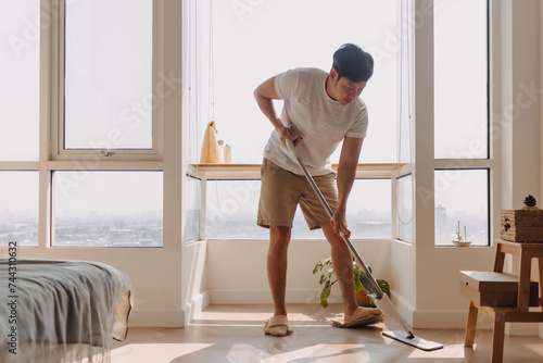 Asian Thai man using mop for cleaning floor in living room apartment, Man do household chores, housework concept. marriage life. photo