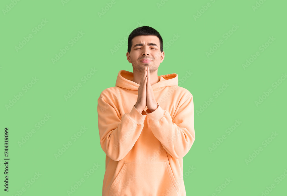 Fototapeta premium Young man praying on green background