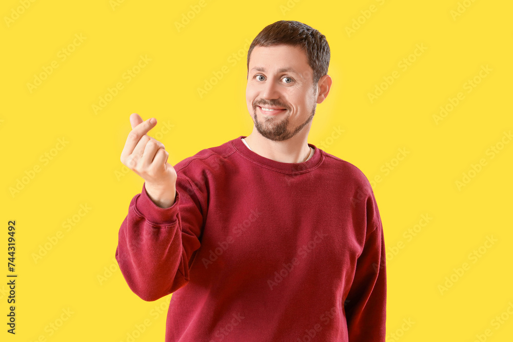 Handsome man making heart gesture on yellow background Handsome man making heart gesture on yellow background