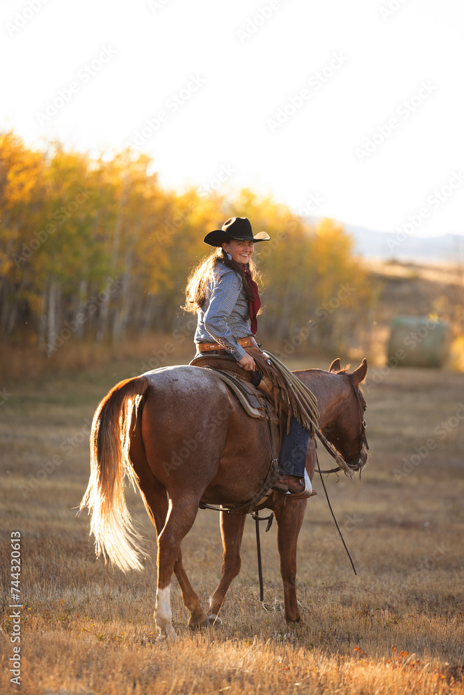 Cowgirl riding roan quarter horse looking back Cowgirl riding roan quarter horse looking back
