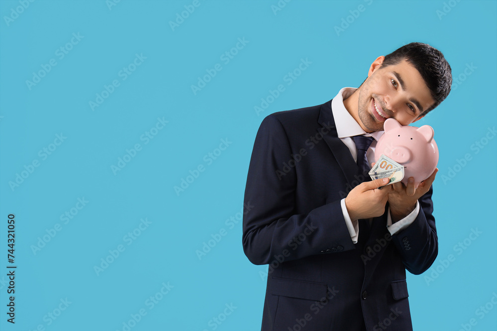 Young businessman with money nd piggy bank on blue background Young businessman with money nd piggy bank on blue background