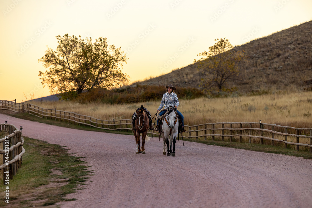 Fototapeta premium Cowgirl riding grey quarter ranch horse leading a horse in the fall