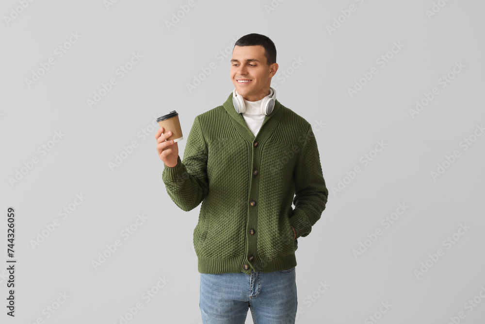 Fototapeta premium Young man in knitted sweater with cup of coffee on light background
