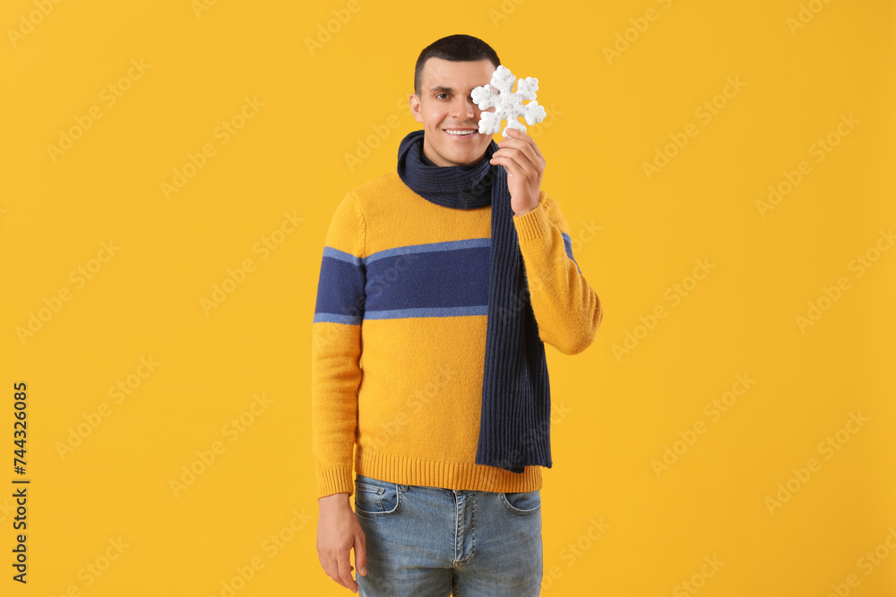 Young man in winter clothes with snowflake on yellow background Young man in winter clothes with snowflake on yellow background