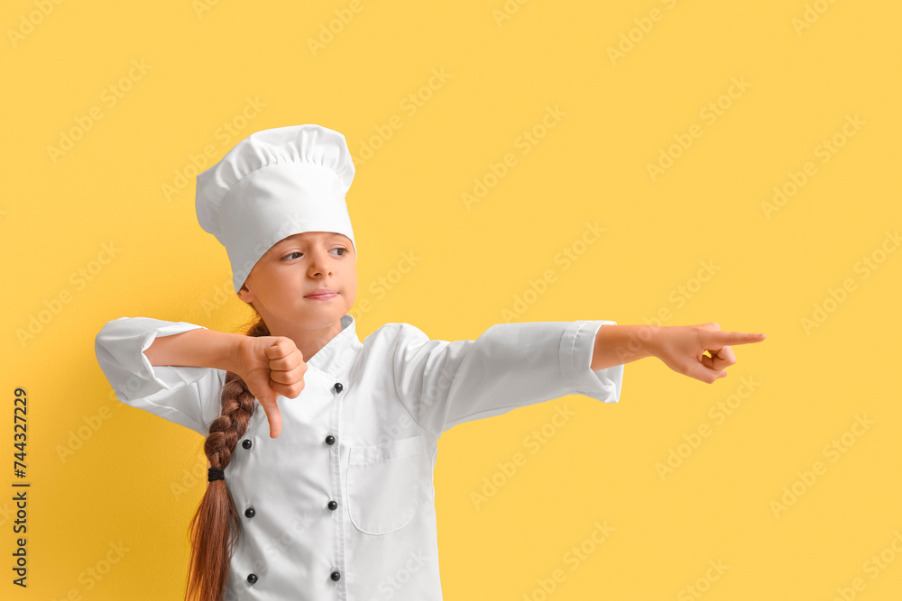 Little chef with dislike pointing at something on yellow background Little chef with dislike pointing at something on yellow background