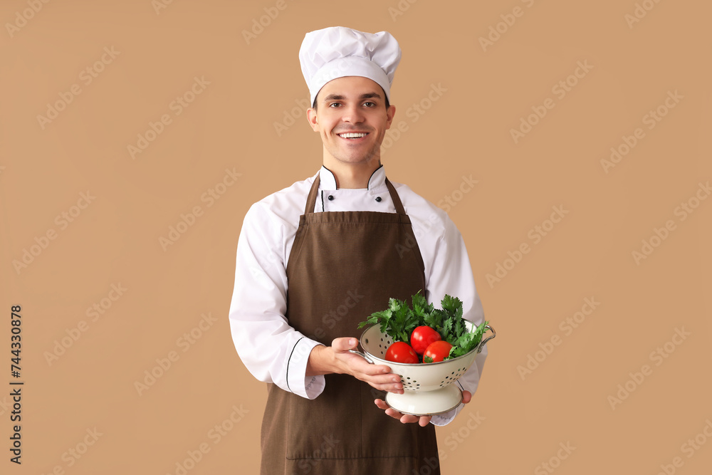 Handsome happy male chef holding colander with fresh vegetables on brown background Handsome happy male chef holding colander with fresh vegetables on brown background