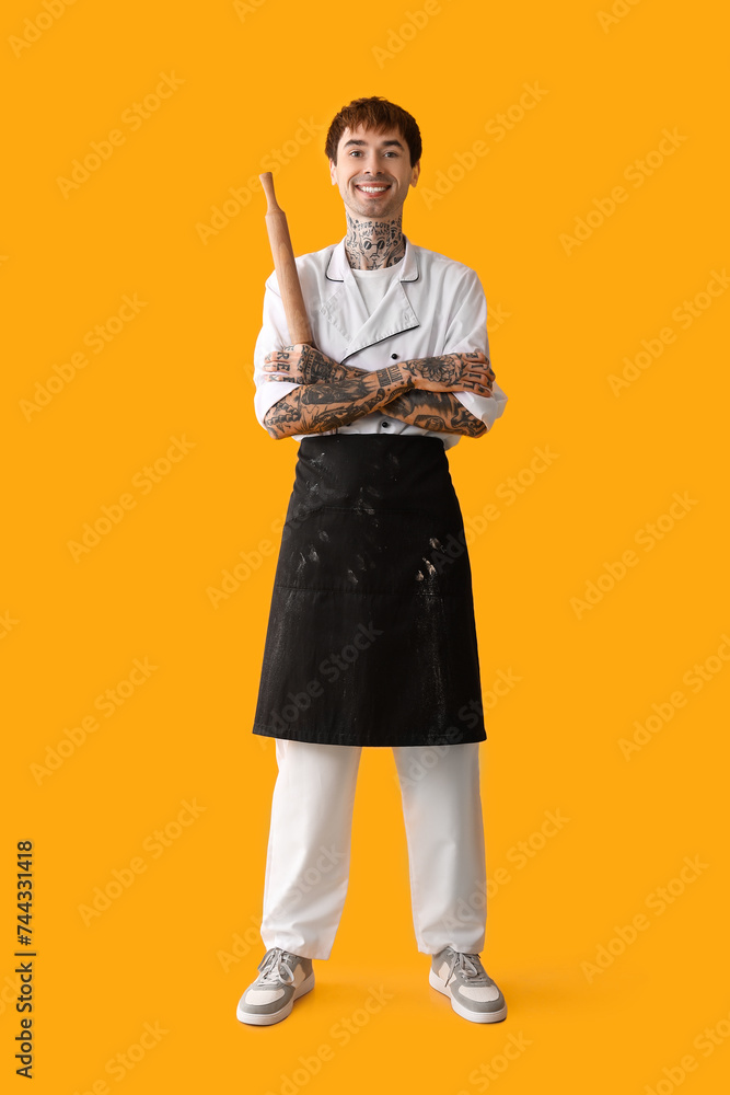 Tattooed happy male chef with rolling pin on yellow background Tattooed happy male chef with rolling pin on yellow background