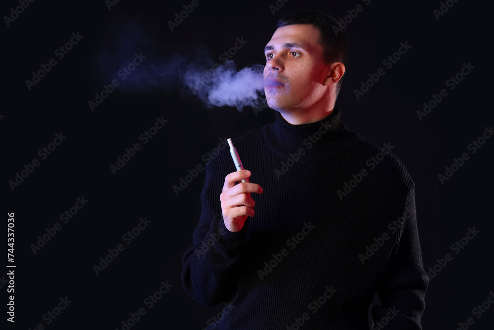 Fototapeta premium Young man smoking electronic cigarette on black background