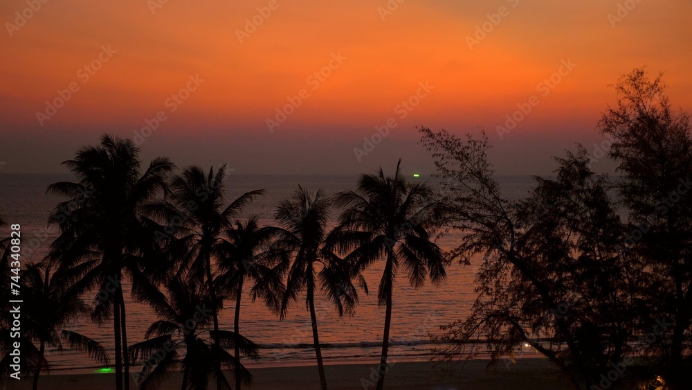 Tropical beach landscape at sunset with silhouette palm trees and tranquil ocean. Vacation and travel background.