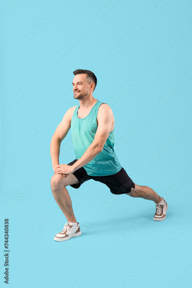 Handsome young happy man in sportswear training on blue background