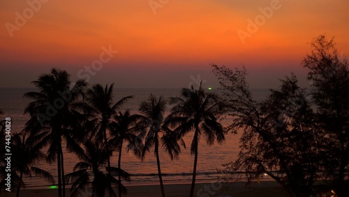 Tropical beach landscape at sunset with silhouette palm trees and tranquil ocean. Vacation and travel background.