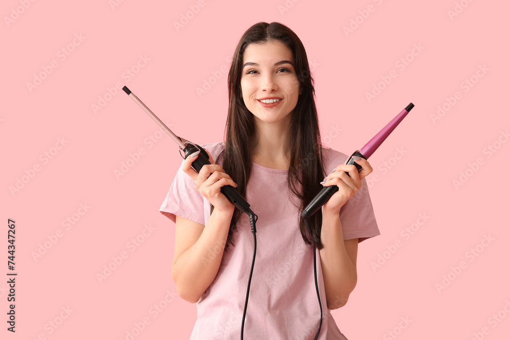 Beautiful young happy woman with curling irons on pink background Beautiful young happy woman with curling irons on pink background