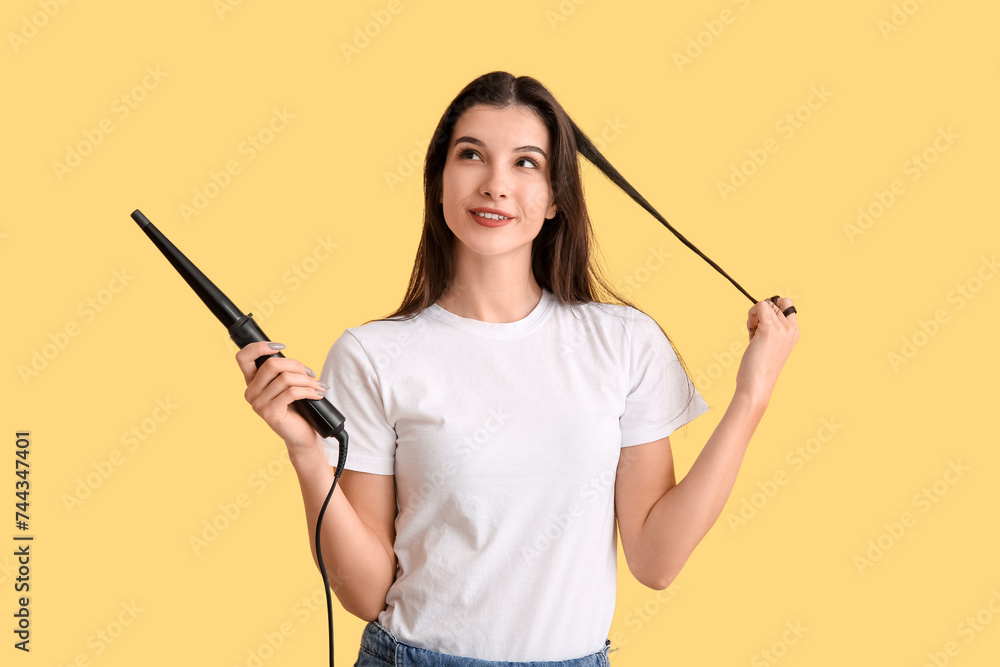 Beautiful young happy woman with curling iron on yellow background Beautiful young happy woman with curling iron on yellow background