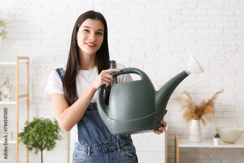 Beautiful young happy female gardener with watering can at home
