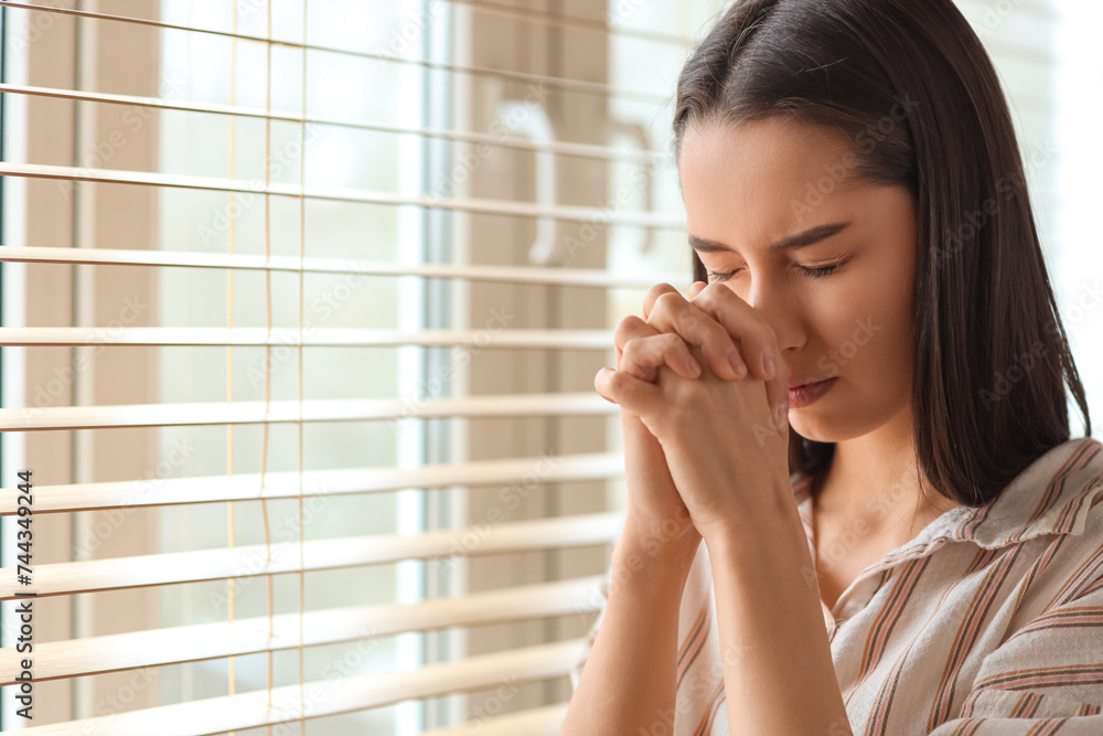 Beautiful young woman praying near window at home Beautiful young woman praying near window at home