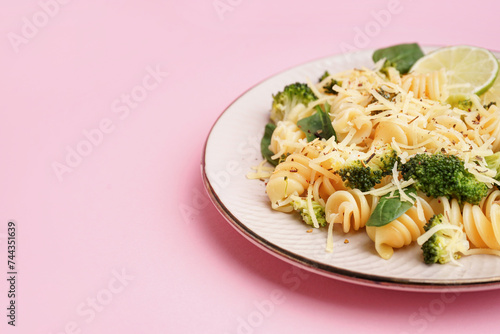Delicious fusilli pasta with broccoli, cheese and lime slices in plate on pink background, closeup