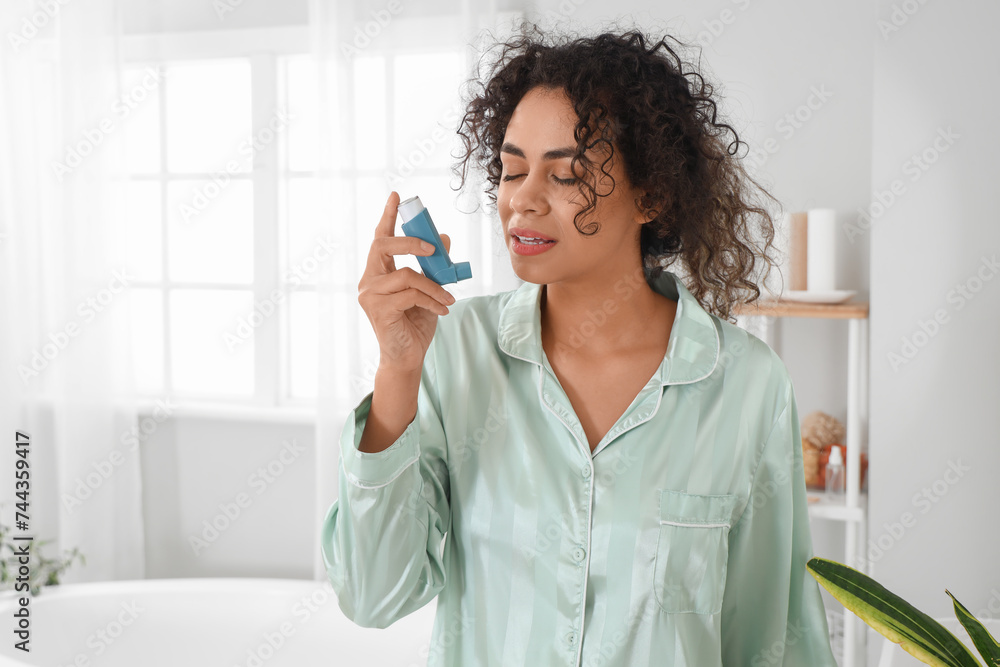 Young African-American woman using asthma inhaler in bathroom Young African-American woman using asthma inhaler in bathroom