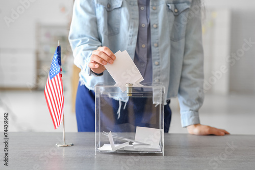 Voting young woman with USA flag near ballot box on table at polling station, closeup