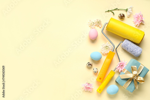 Composition with paint rollers, gift box, flowers and Easter eggs on color background